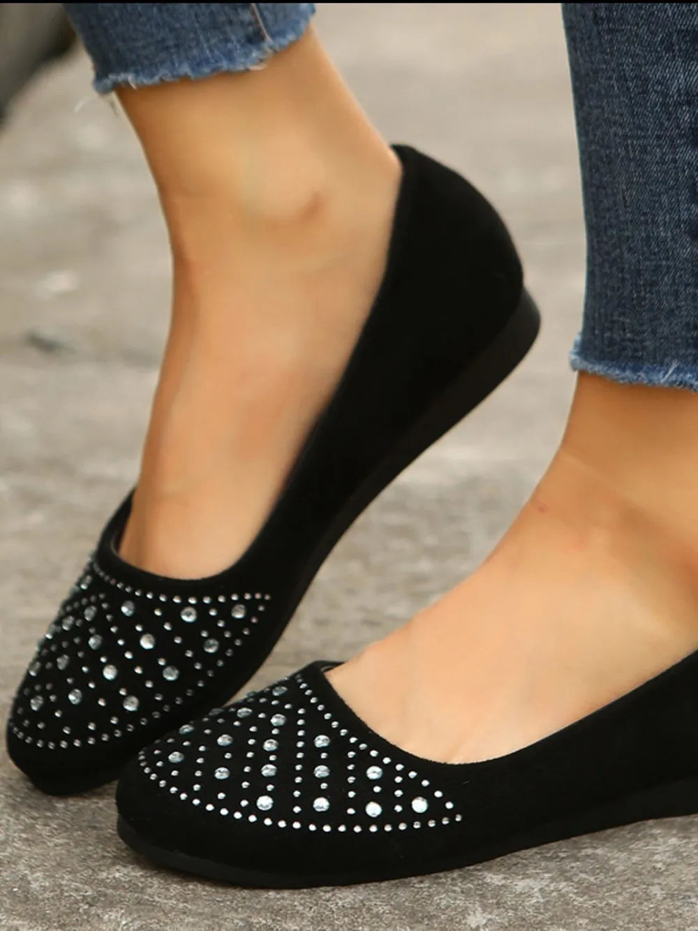 Black suede ballet flats with rhinestone embellishments, styled with jeans.