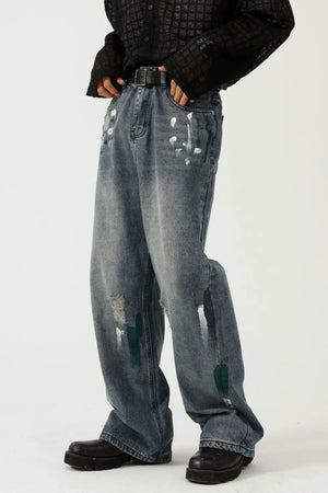 Medium wash baggy jeans with white and green paint splatters and distressed details.