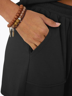 Black drawstring shorts with pockets, shown on a model wearing bracelets.