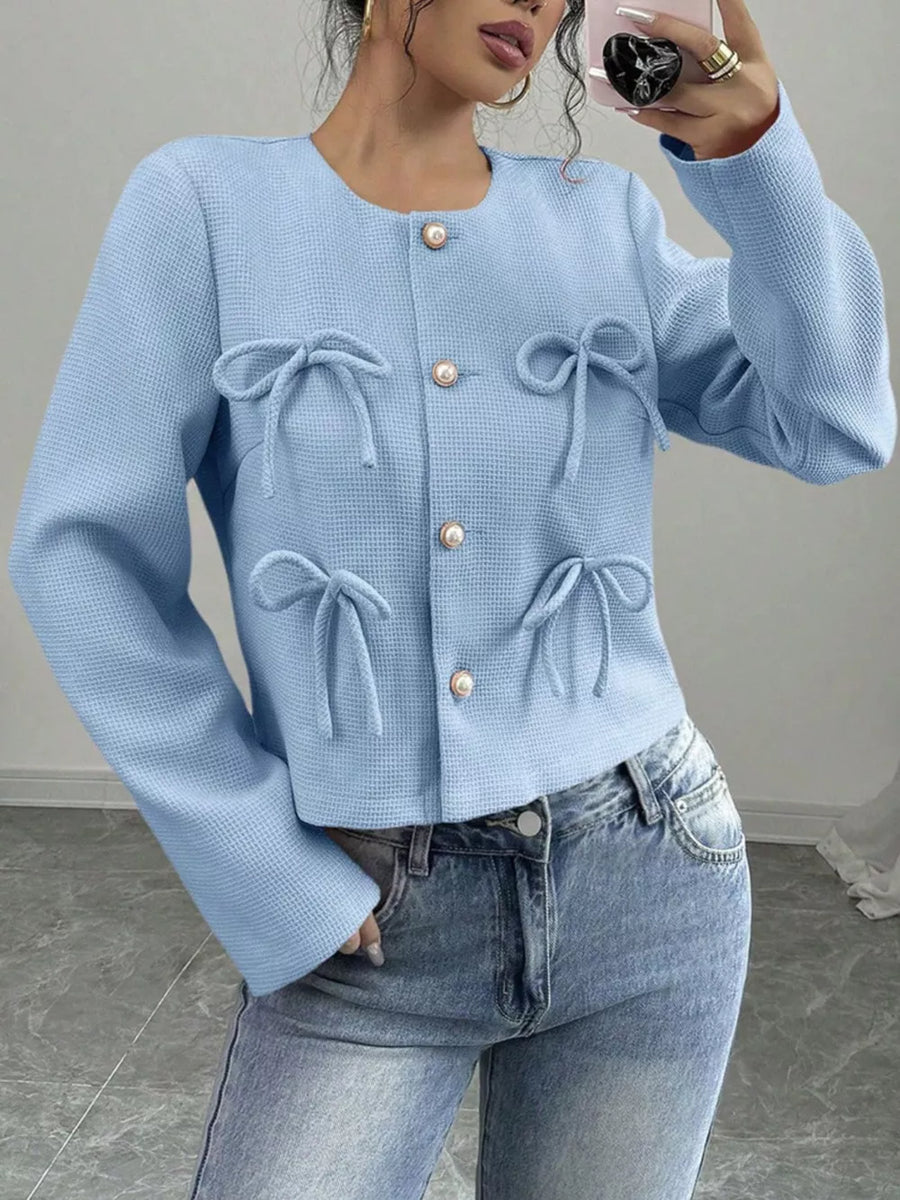 Light blue textured cropped jacket with pearl buttons and bow details.