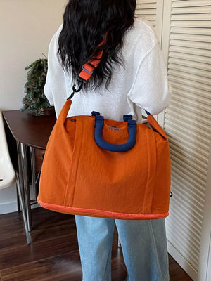 Spacious orange Oxford cloth travel bag with blue handles and orange trim, worn over the shoulder.