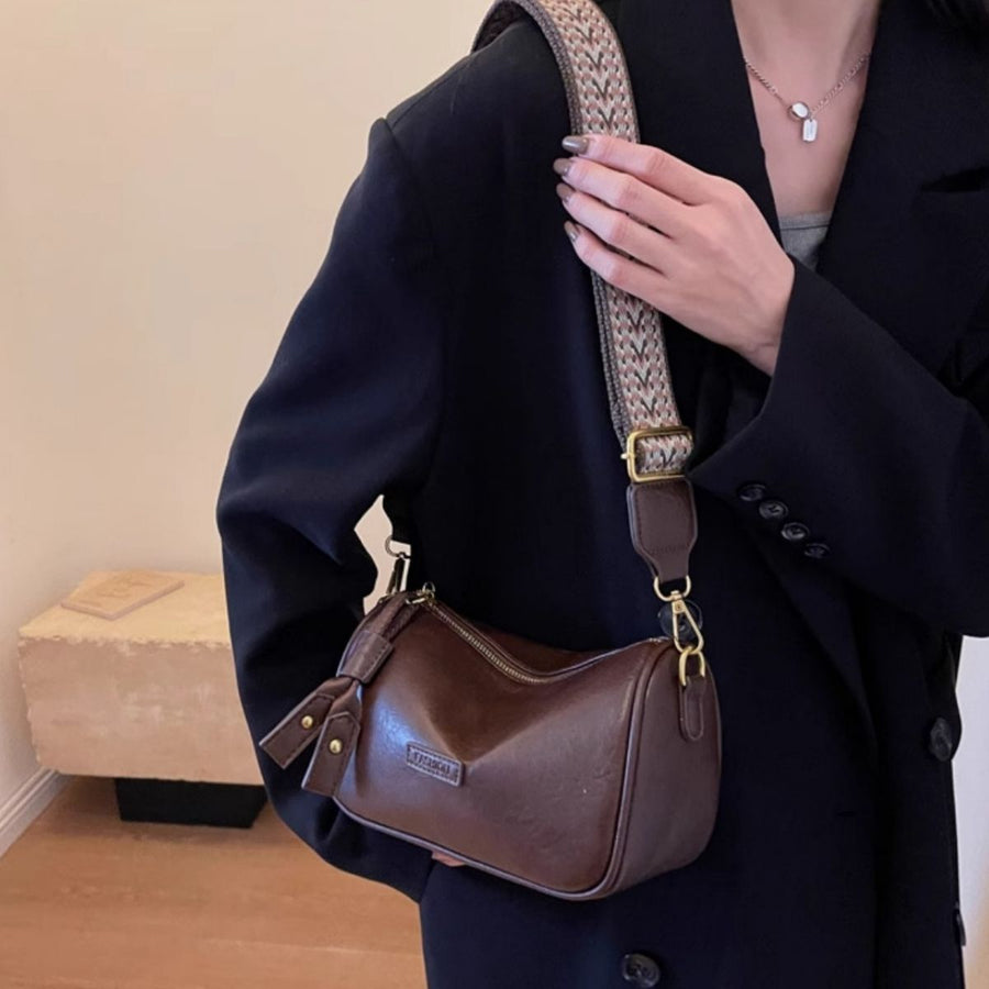 Brown textured PU leather crossbody bag with tassel detail and woven strap.