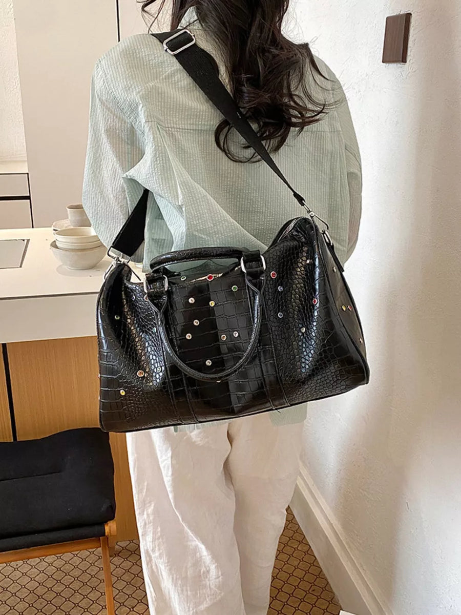 Black crocodile textured duffel bag with studded details and detachable strap.