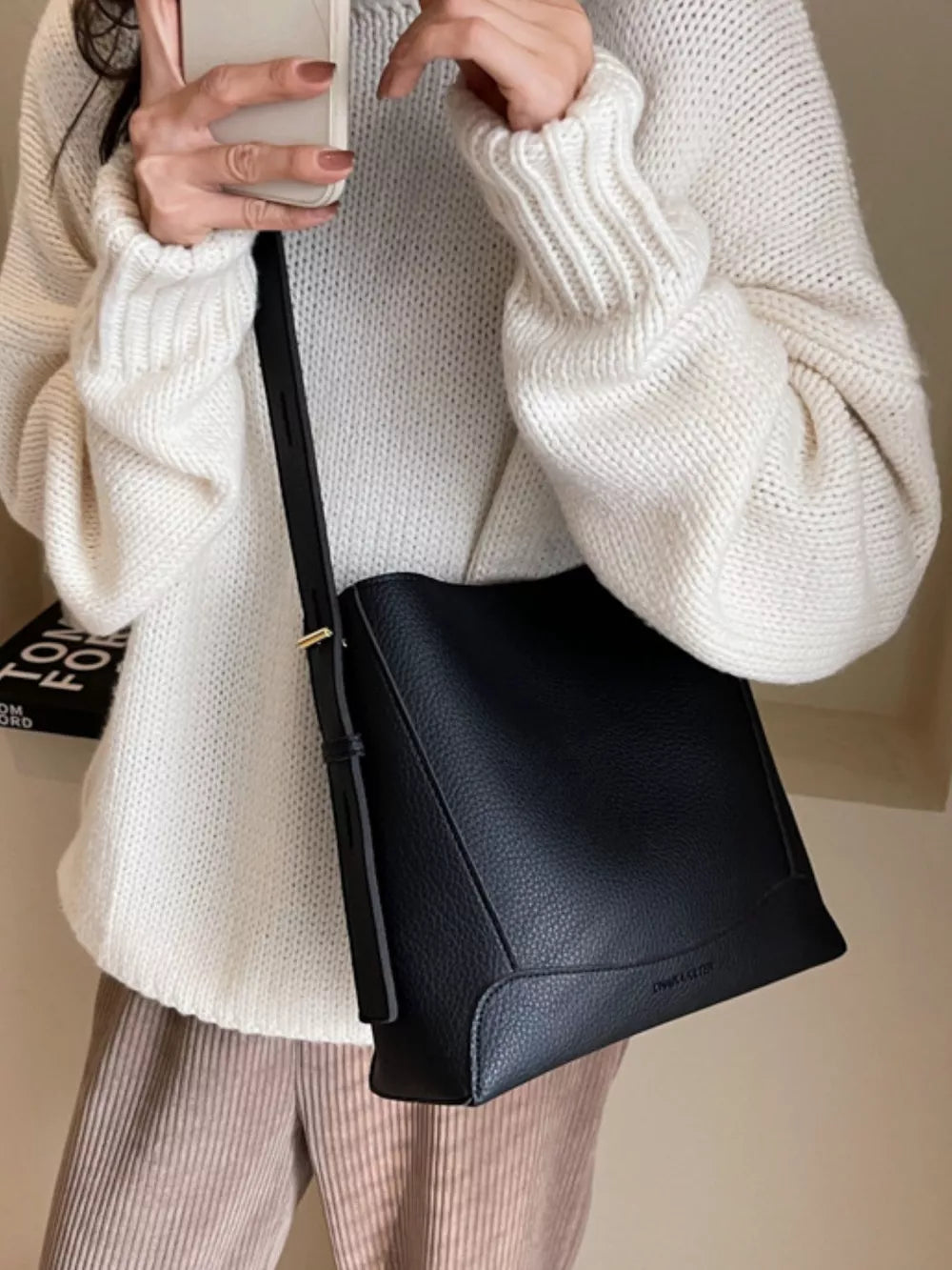 Black pebbled leather crossbody bag with adjustable strap and embossed logo detail.