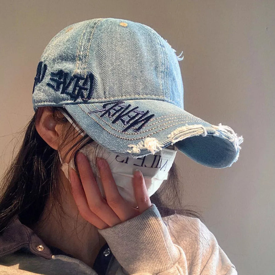 Denim blue distressed baseball cap with dark embroidery and frayed details.