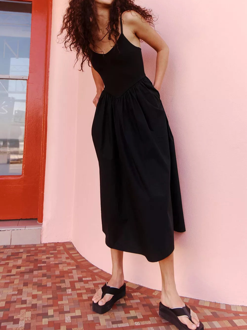 Black midi dress with spaghetti straps, defined waist, and pockets.
