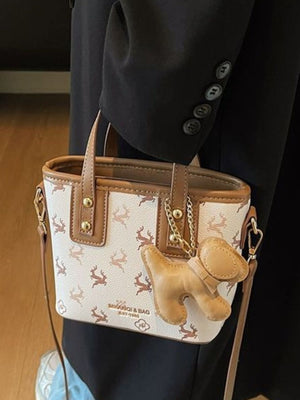 Charming mini crossbody bag with deer print and dog charm, in white with brown trim.