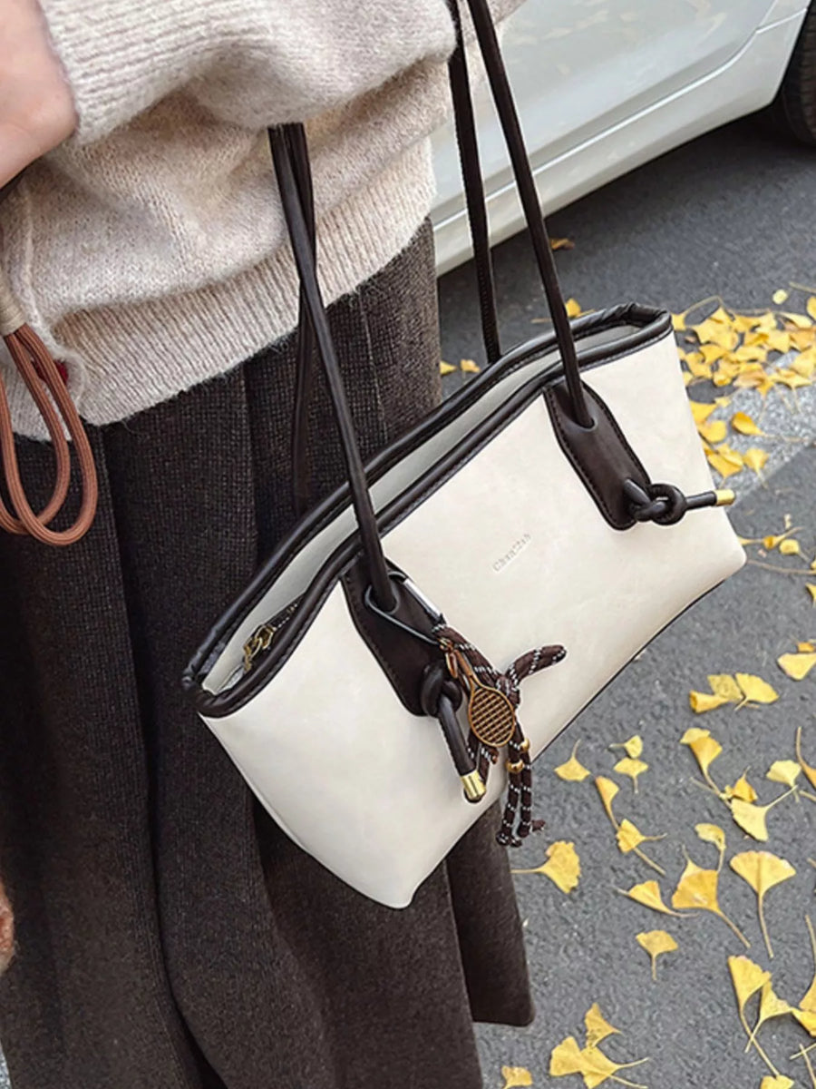 White leather shoulder bag with brown trim and tennis racket charm.