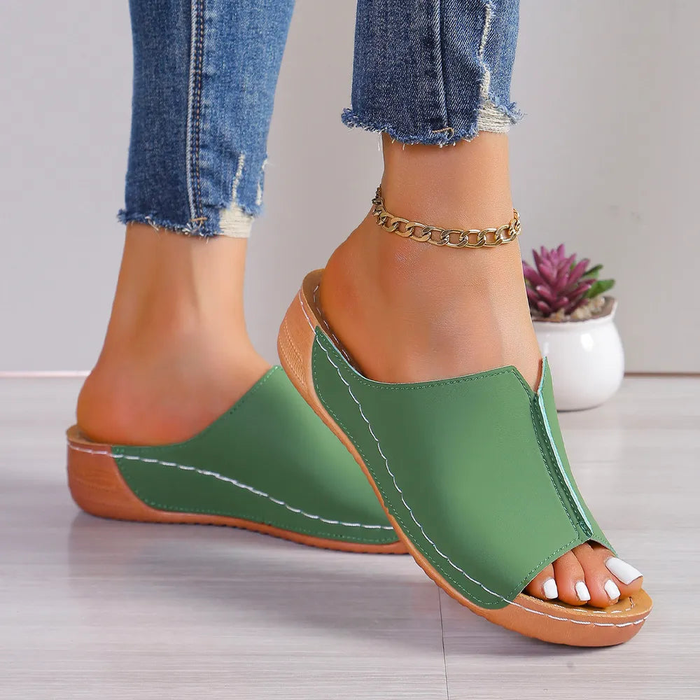 Green stitched edge wedge mules with peep toe and wooden heel detail.