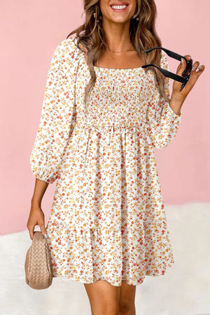 Floral smocked mini dress with square neckline and puff sleeves in beige with orange and yellow floral print.