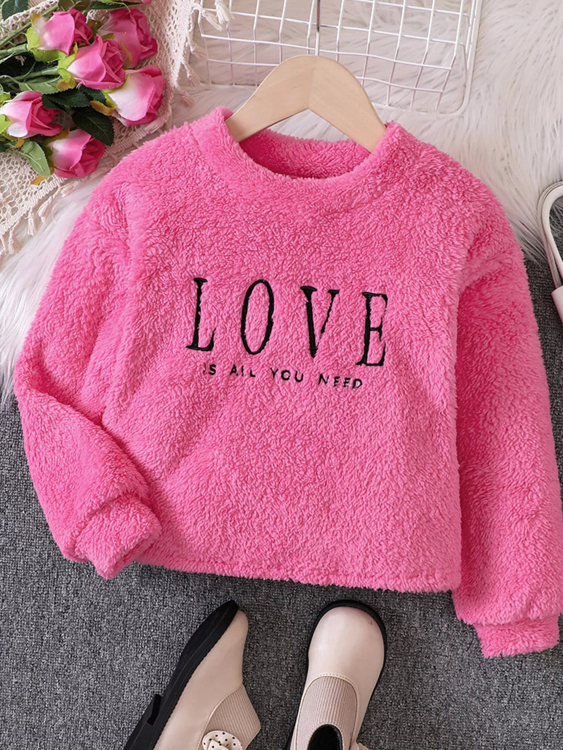 Fuzzy pink sweatshirt for kids with black "LOVE IS ALL YOU NEED" graphic.
