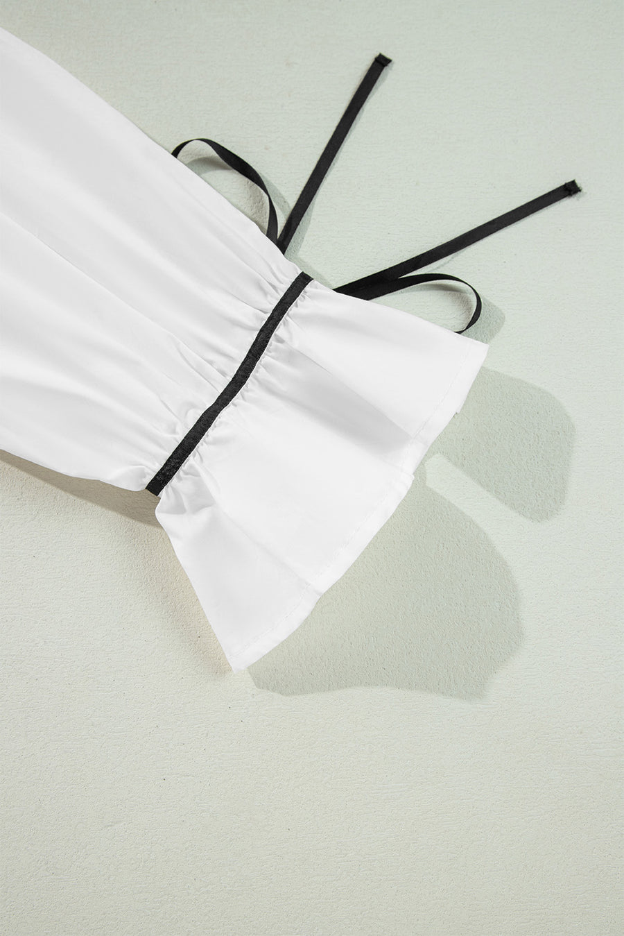 White blouse with black piped trim and tie detail on sleeve cuff