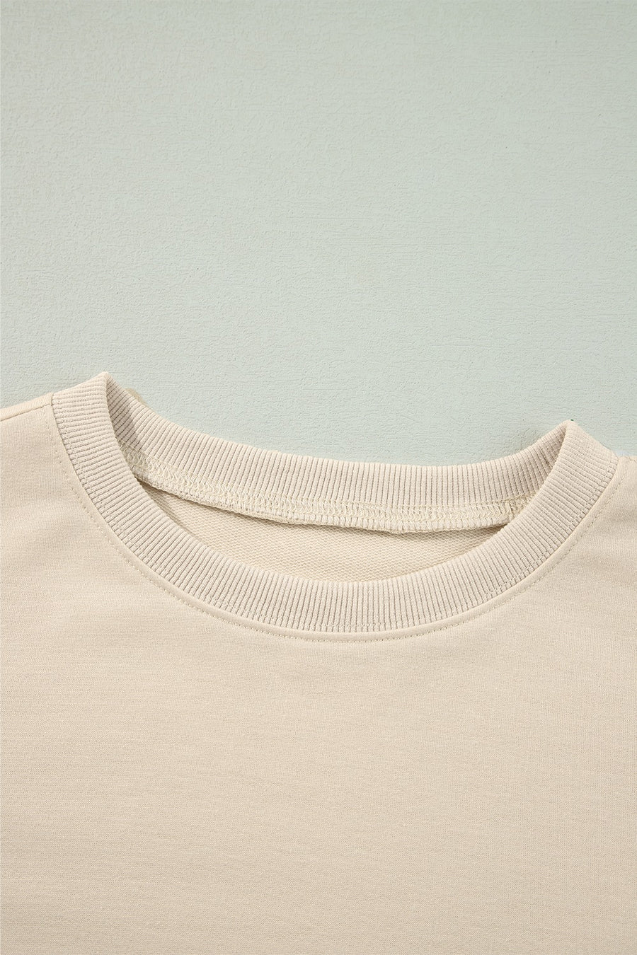 Cream sweatshirt with ribbed crew neck and visible stitching detail.