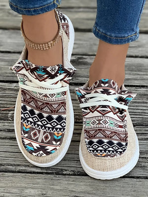 Aztec print canvas slip-on flats in tan with a white sole and decorative ankle bracelet.