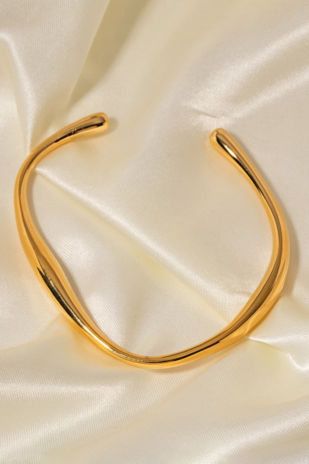 Gold 18K gold-plated open-ended bangle with a sculpted, fluid design on satin.