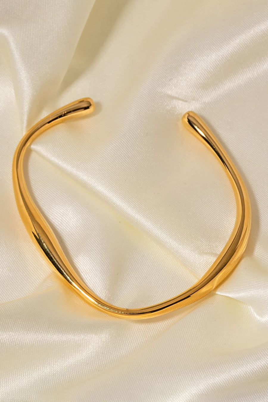 Gold 18K gold-plated open-ended bangle with a sculpted, fluid design on satin.