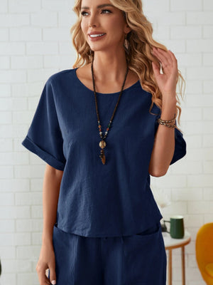 Dark blue linen co-ord top with cuffed short sleeves and round neck, styled with a beaded necklace.