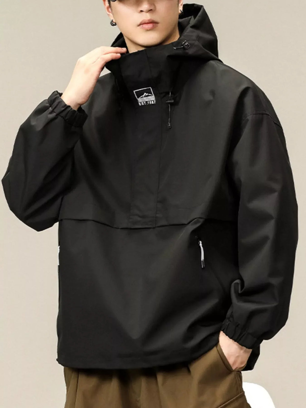 Black oversized hooded windbreaker jacket with a chest logo and zippered pocket.