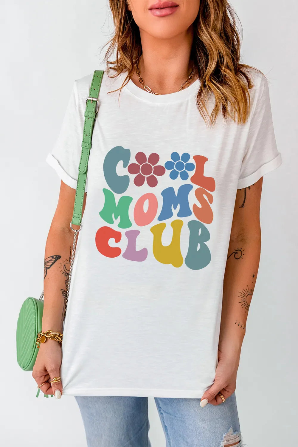 White graphic t-shirt with colorful retro text that reads "Cool Moms Club" and floral accents.