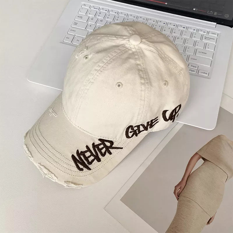 Cream white distressed cotton baseball cap with embroidered "Never Give Up" text.
