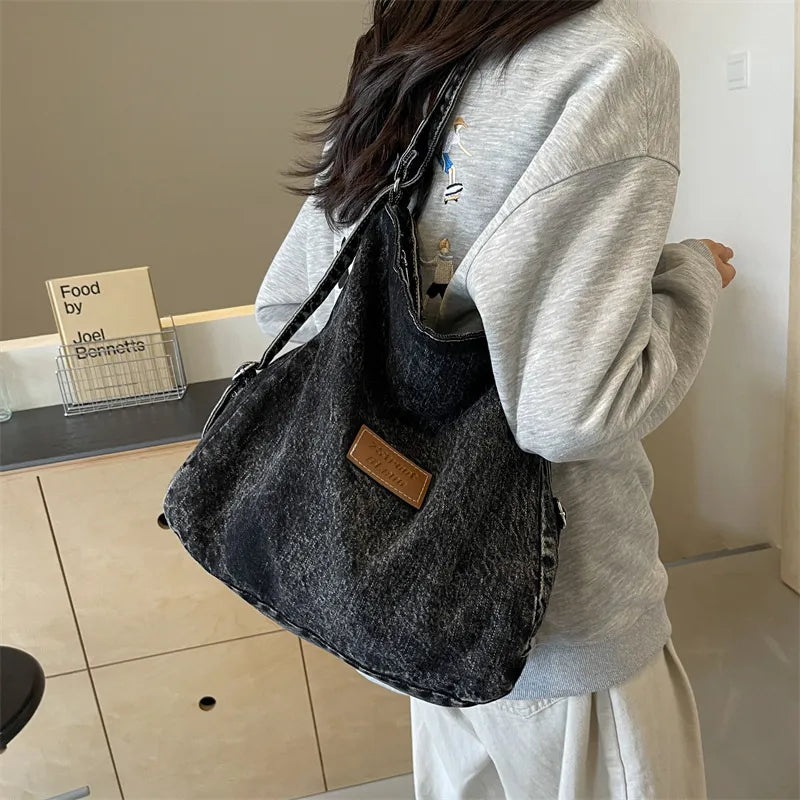 Black denim hobo bag with leatherette patch and adjustable strap.