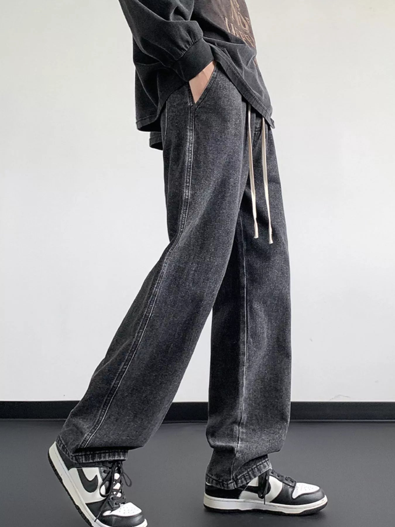 Oversized dark gray denim jeans with drawstring waist and loose fit.