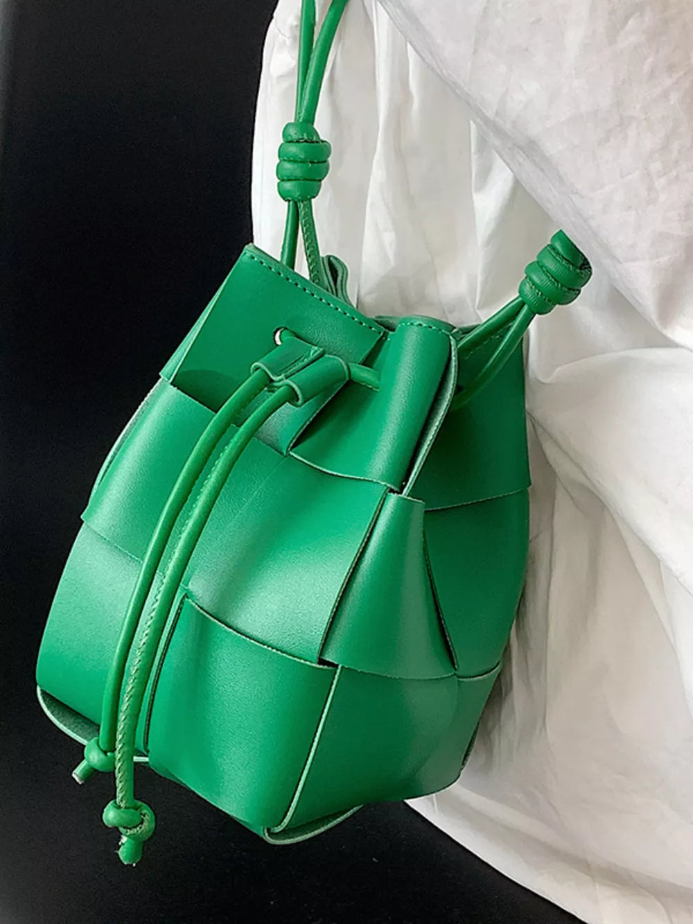 Green woven mini bucket bag with drawstring closure and knotted strap detail.