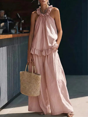 Pink ruffled halter neck top and wide-leg pants set with a straw tote bag.