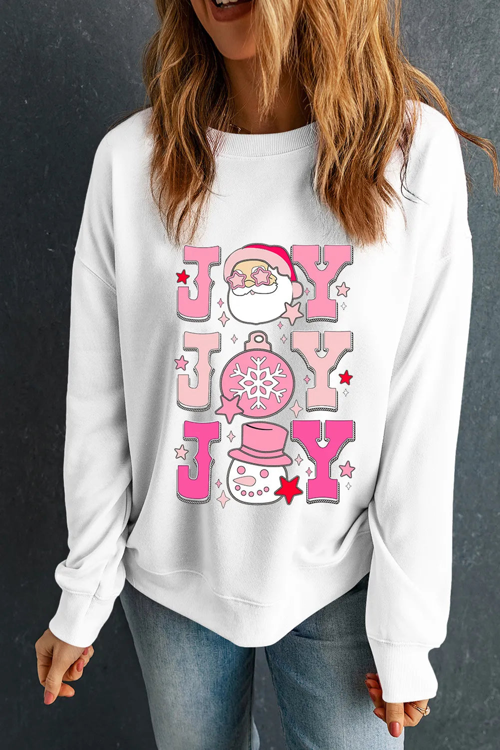 White crewneck sweatshirt with a pink graphic featuring Santa, snowflake ornament, and snowman spelling JOY.