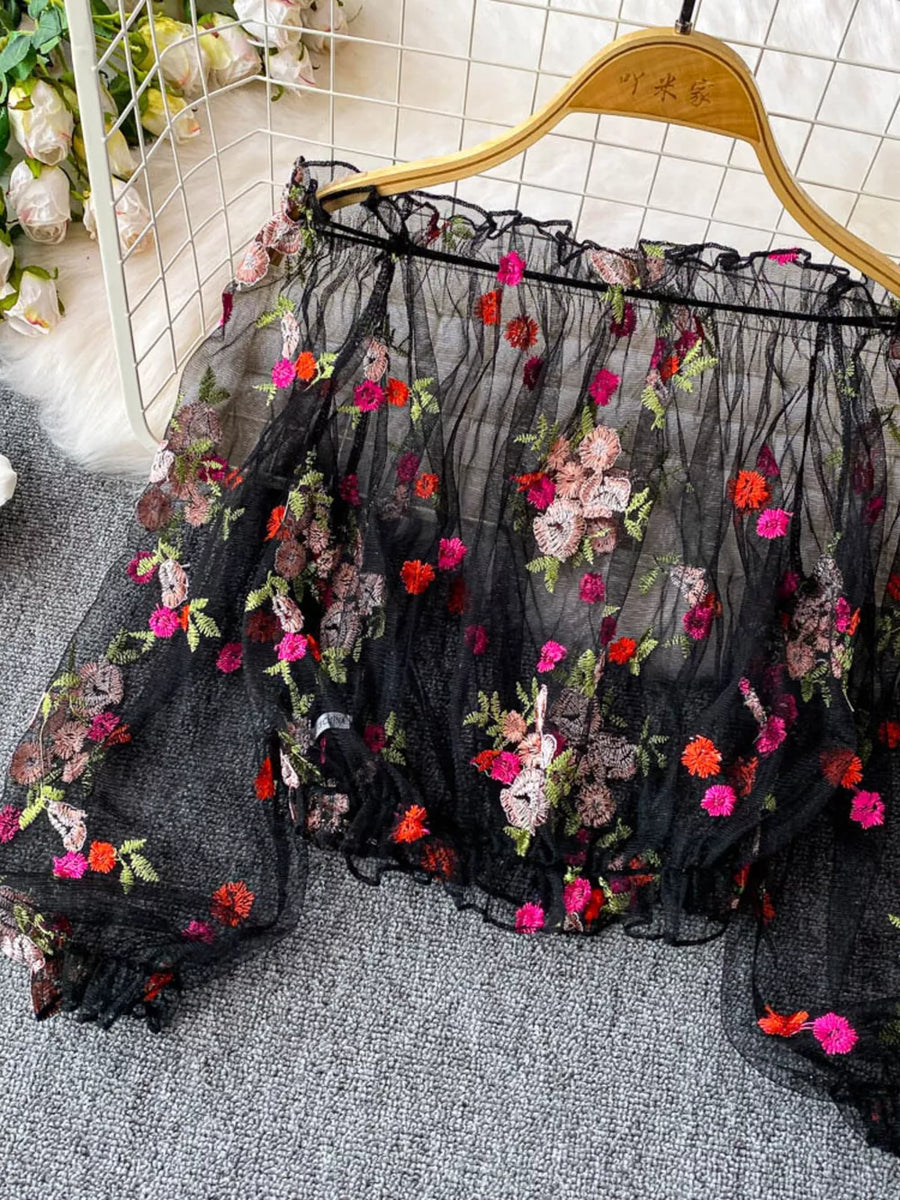 Black off-shoulder t-shirt with colorful floral embroidery and ruffled neckline.