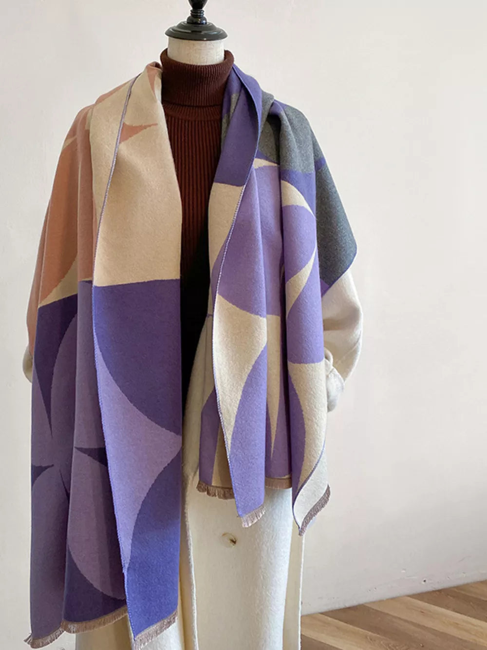 Geometric patterned soft scarf with fringes in purple, beige, and pink, featuring a fringed hem.