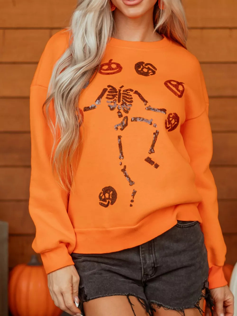 Orange crewneck sweater featuring sequin embellishment and graphic