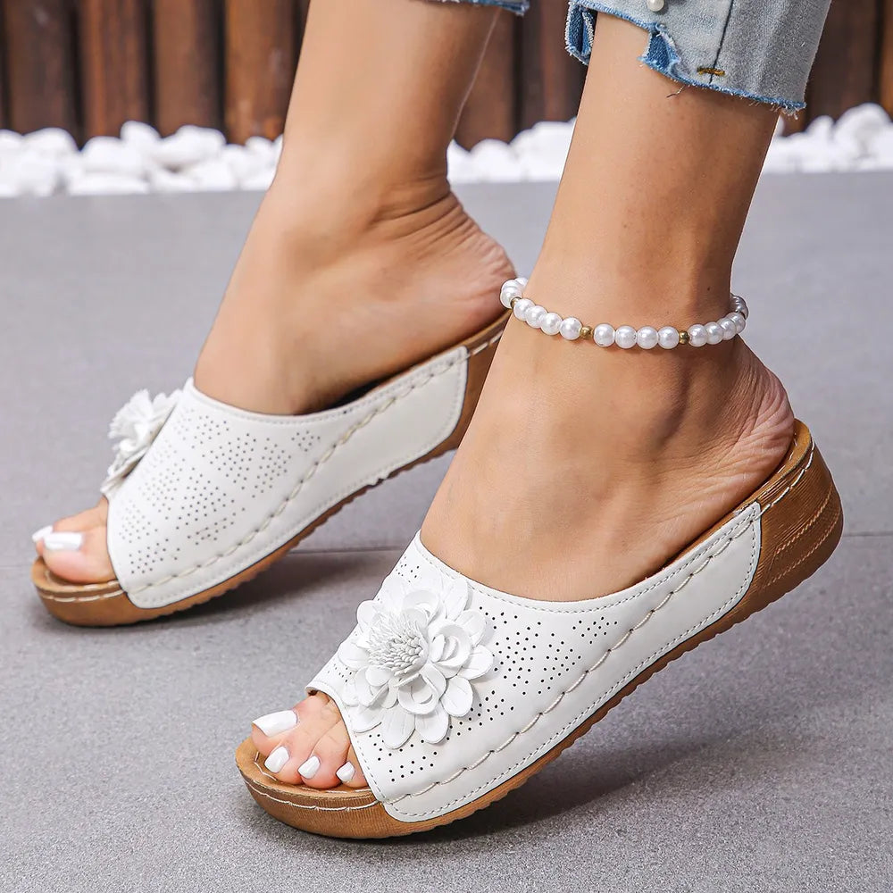 White perforated floral wedge slides with open toe and cork sole detail.