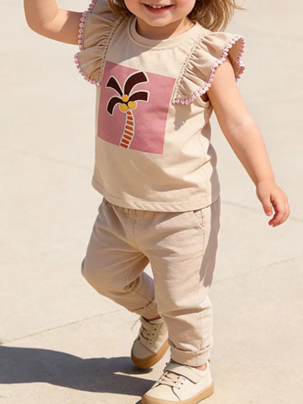 Baby girls' tan cotton tee with playful palm tree graphic and pink pom-pom ruffle sleeves.
