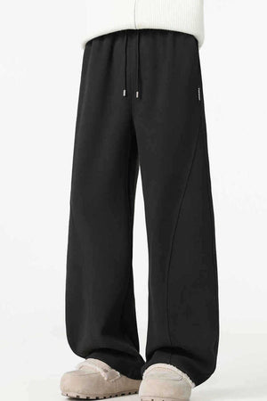 Black relaxed wide-leg sweatpants with drawstring and curved seam detail.