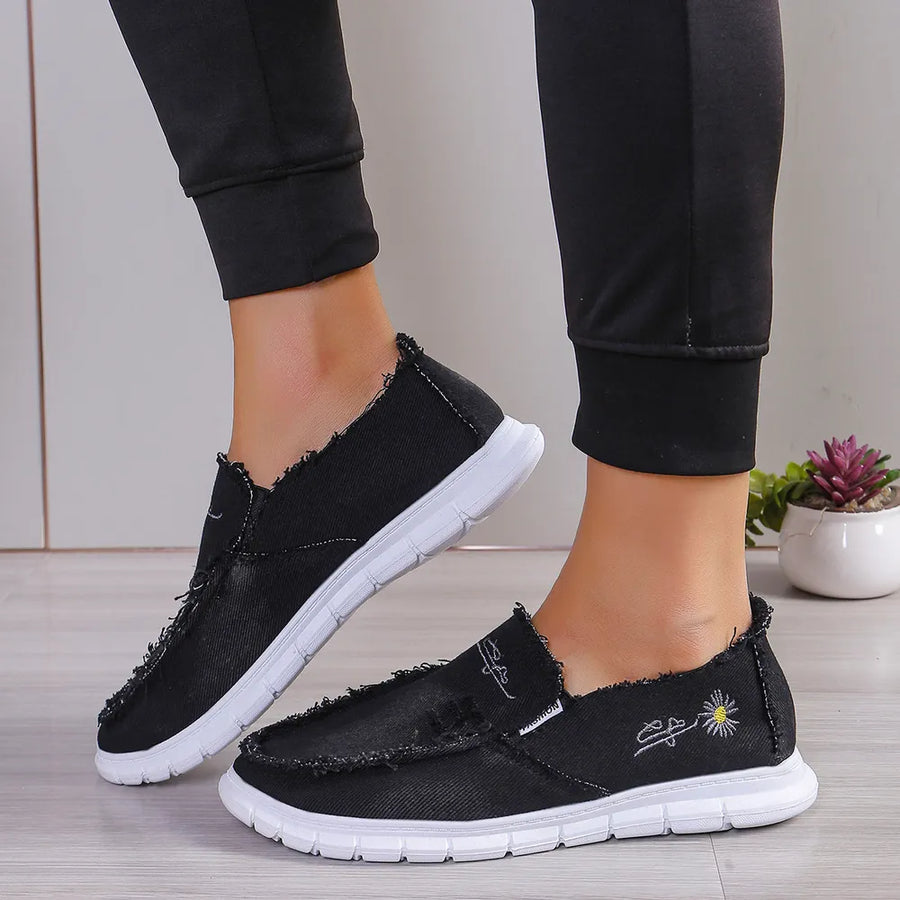 Black canvas slip-on shoes with raw edges and embroidered details.