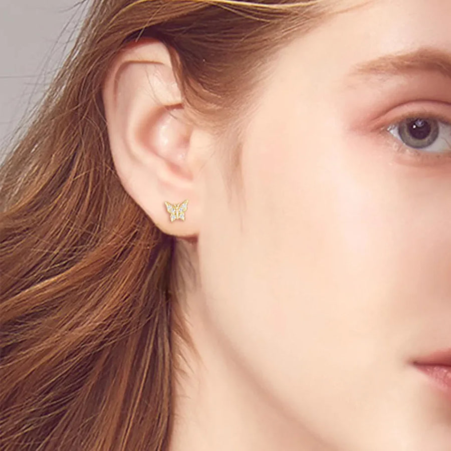 Gold moissanite butterfly stud earrings with clear stones, shown on ear.