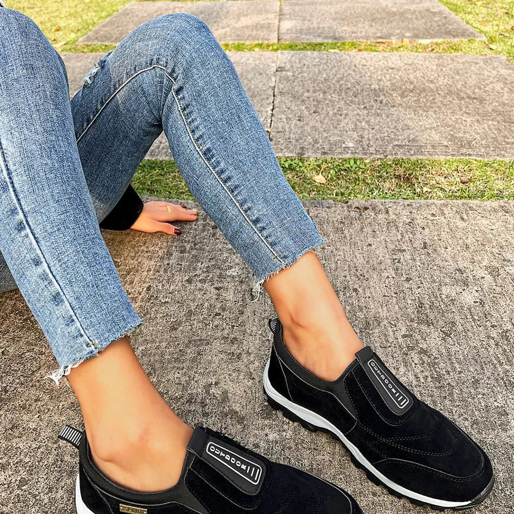 Black suede-like round toe slip-on sneakers with elastic side panels and white soles.
