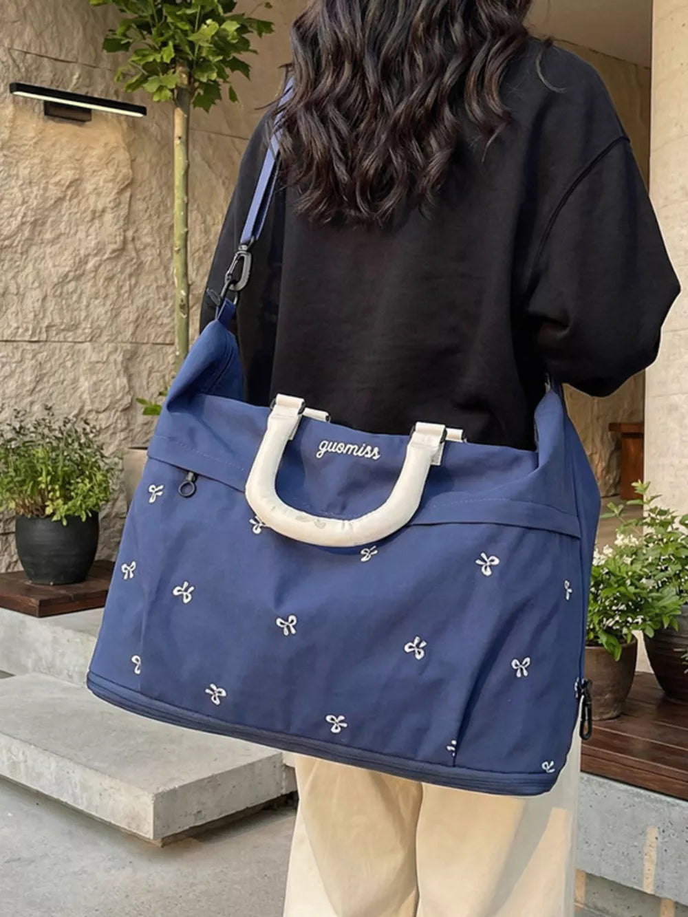 Blue duffel bag with white bow pattern and white handles, worn over the shoulder.