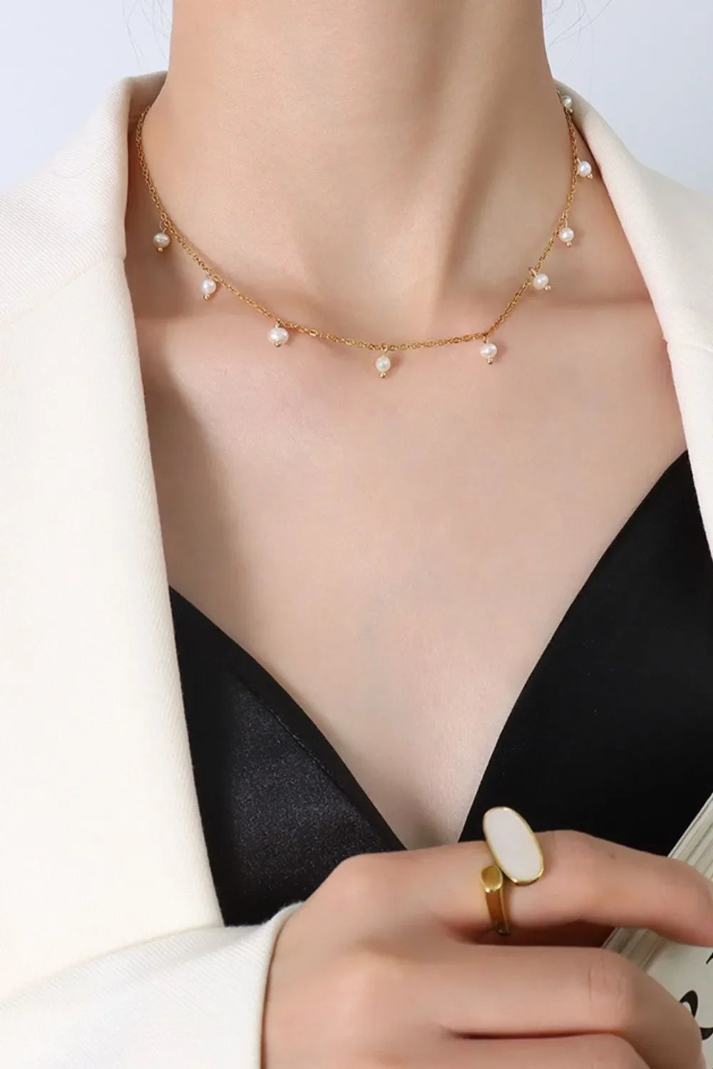Gold chain necklace with dangling pearl accents, worn at the collarbone.