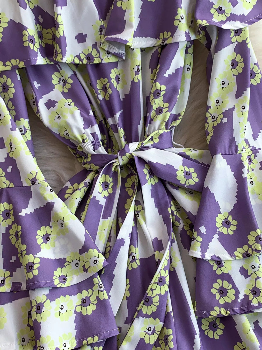 Purple floral print off-shoulder ruffled romper with tie waist and bell sleeves.