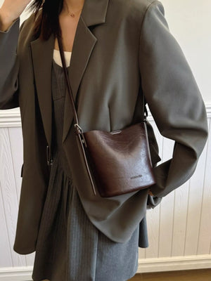 Chocolate leather bucket crossbody bag with embossed logo detail.