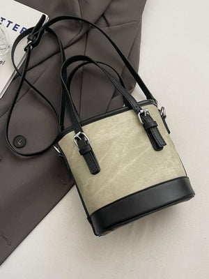Two-tone bucket crossbody bag in beige canvas with black trim and straps.