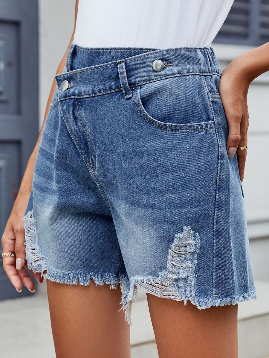 Medium wash denim shorts with asymmetric wrap, shredding and frayed hem.