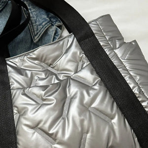 Padded silver nylon tote bag with black straps and exterior pockets, featuring a quilted pattern.