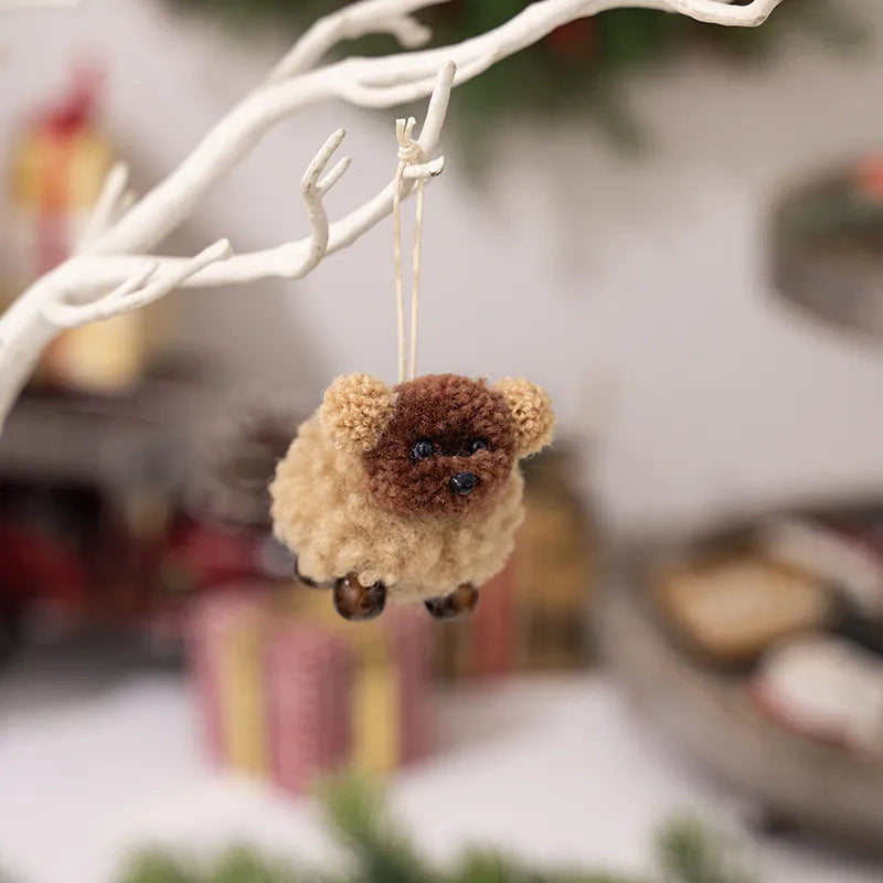 Woolly sheep ornament with pom-pom ears, brown and tan, with bead feet, hanging on a branch.