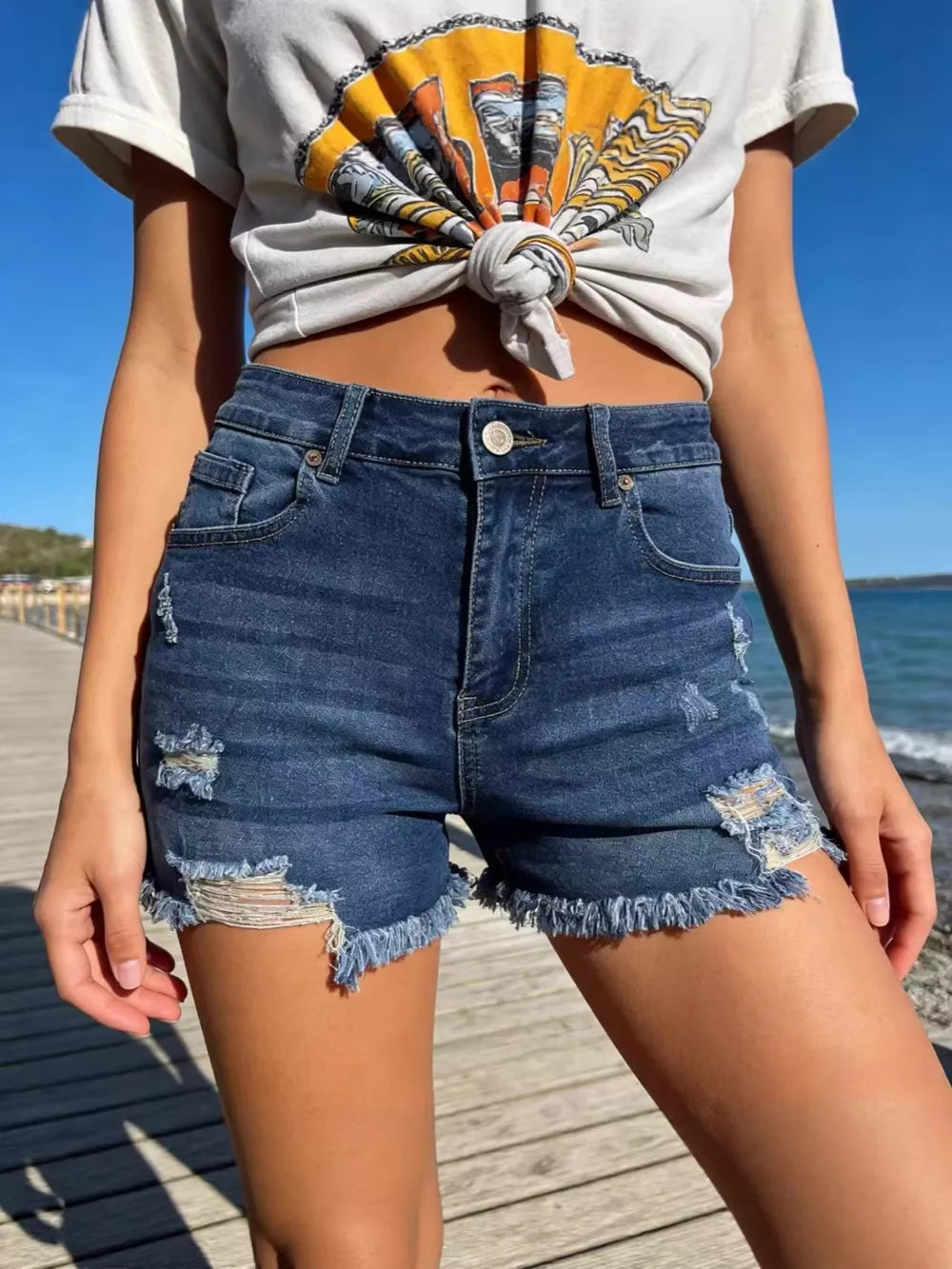 Distressed dark blue denim shorts with raw frayed hem and button fly.