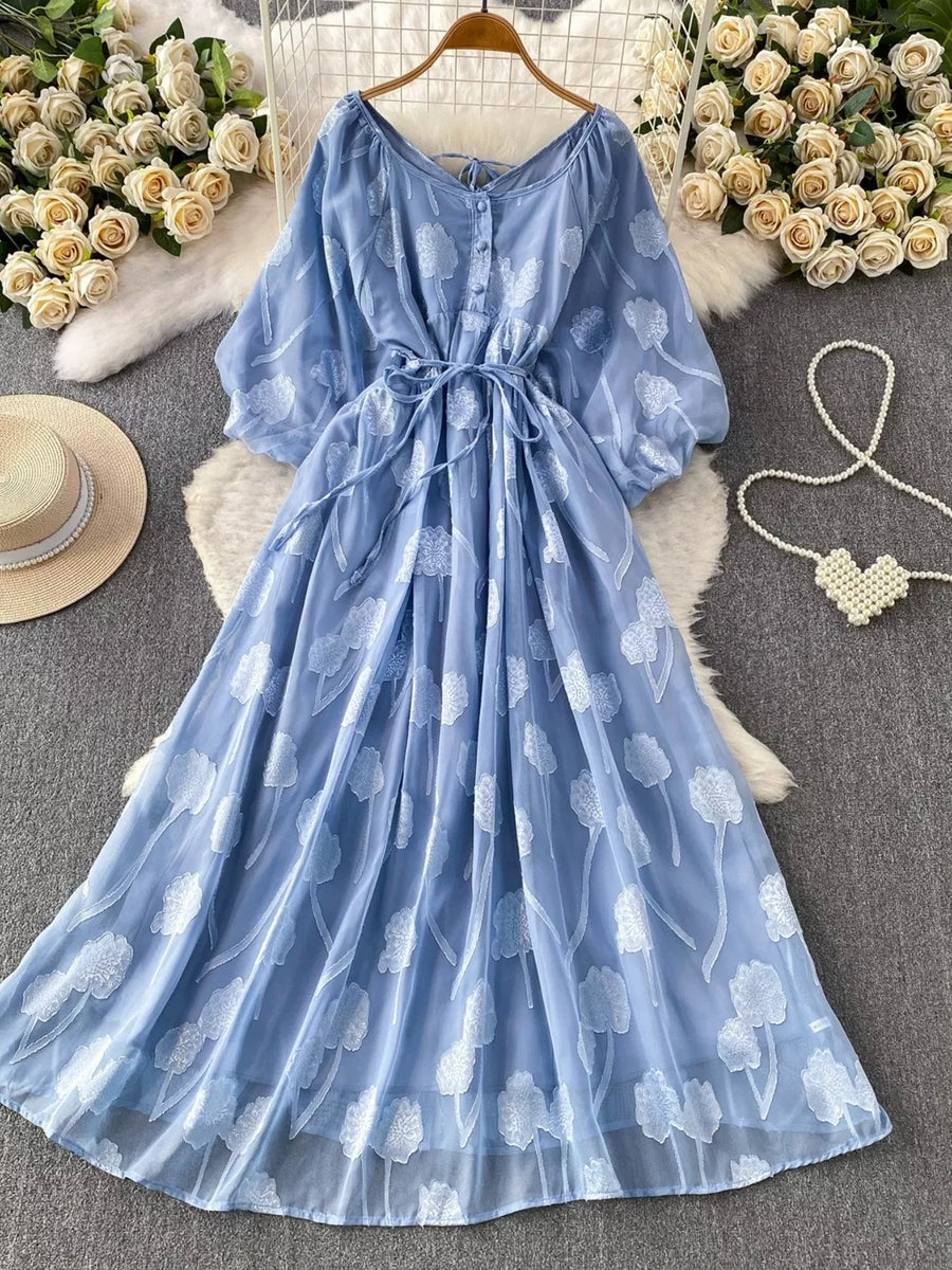Blue chiffon maxi dress with floral embroidery, V-neck, button front, and belted waist.
