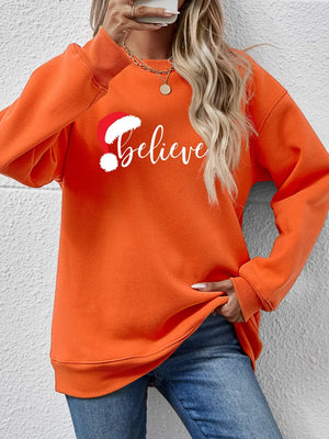 Orange raglan sweatshirt with white "Believe" graphic and Santa hat detail
