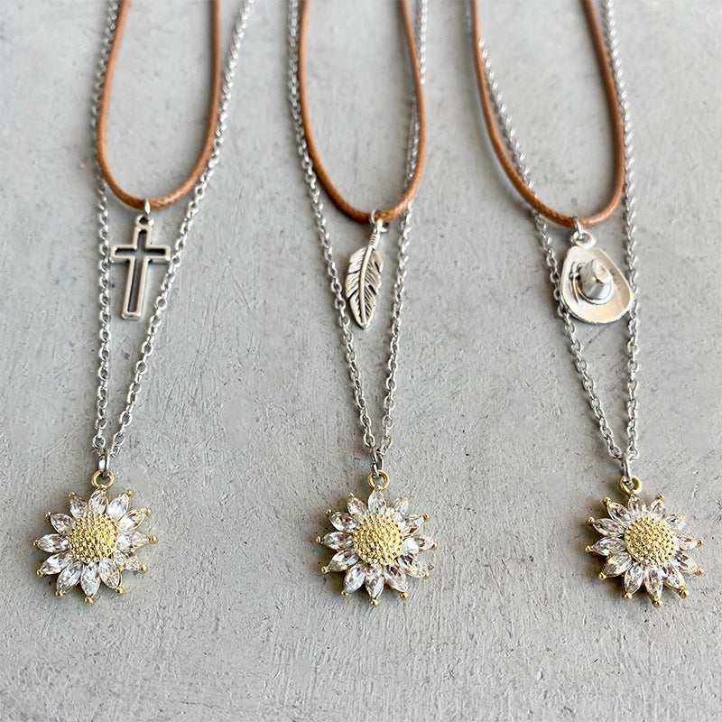 Layered sunflower charm necklaces with cross, feather, and cowboy hat pendants.
